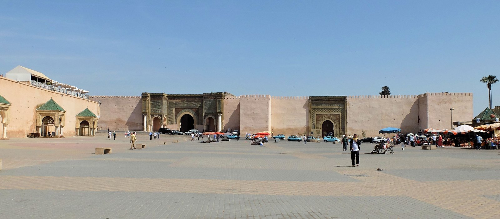 Place el-Hedim square in Meknes looking toward the monumental Bab Mansour gate, with its green-and-white zellij tilework and horseshoe arch